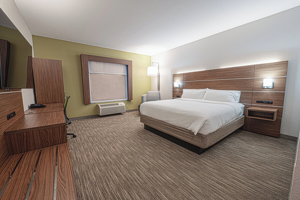 A hotel room with a bed, a desk, a chair, a lamp, and a window.