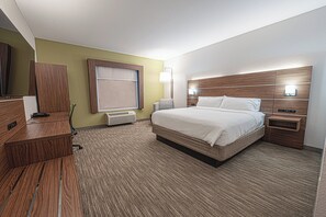 Une chambre d’hôtel comprenant un lit, des tables de chevet, un bureau, une chaise, une fenêtre avec stores et une lampe fixée au mur.