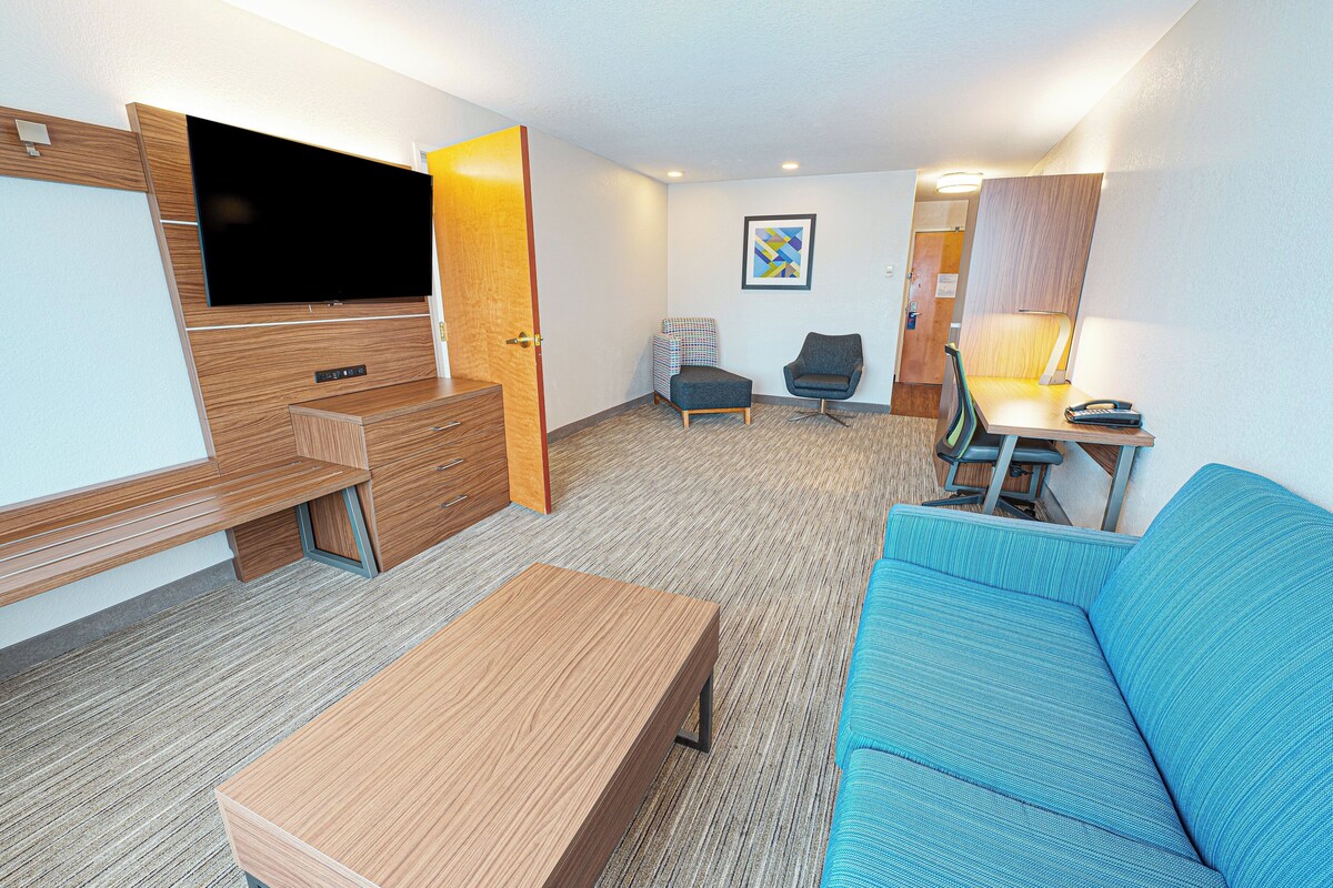 A compact hotel room with a sofa, a small table, a TV, a desk, and a chair.