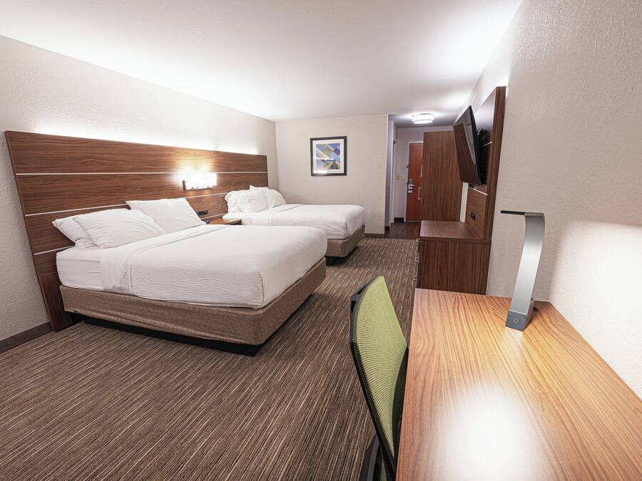 A hotel room with two beds, a desk, a chair, and a staircase.