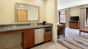 A compact hotel room with a kitchenette, a flat-screen TV, a dining area, and a large window with curtains. - Hampton Inn & Suites Birmingham East Irondale (Birmingham)