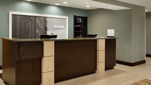 A reception desk with a 'travel' sign, a counter, and a small shelf with items. - Hampton Inn & Suites Birmingham East Irondale (Birmingham)