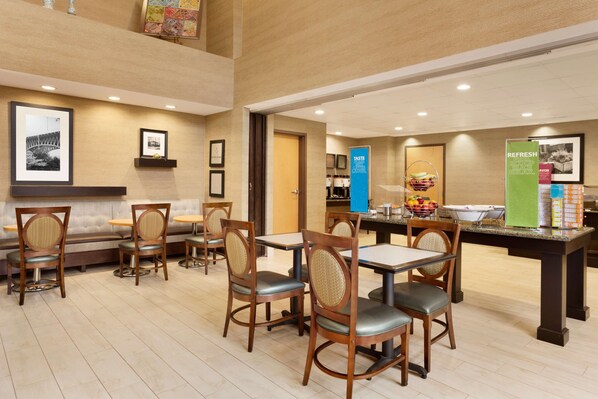 Un comedor de hotel con sillas y mesas de madera, un mostrador de buffet y cuadros en las paredes.