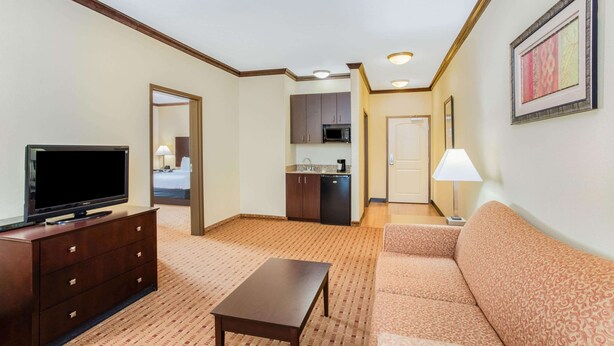 Une chambre d’hôtel équipée d’une télévision, d’un canapé, d’une petite table, d’un coin cuisine et d’une porte donnant sur une autre pièce.