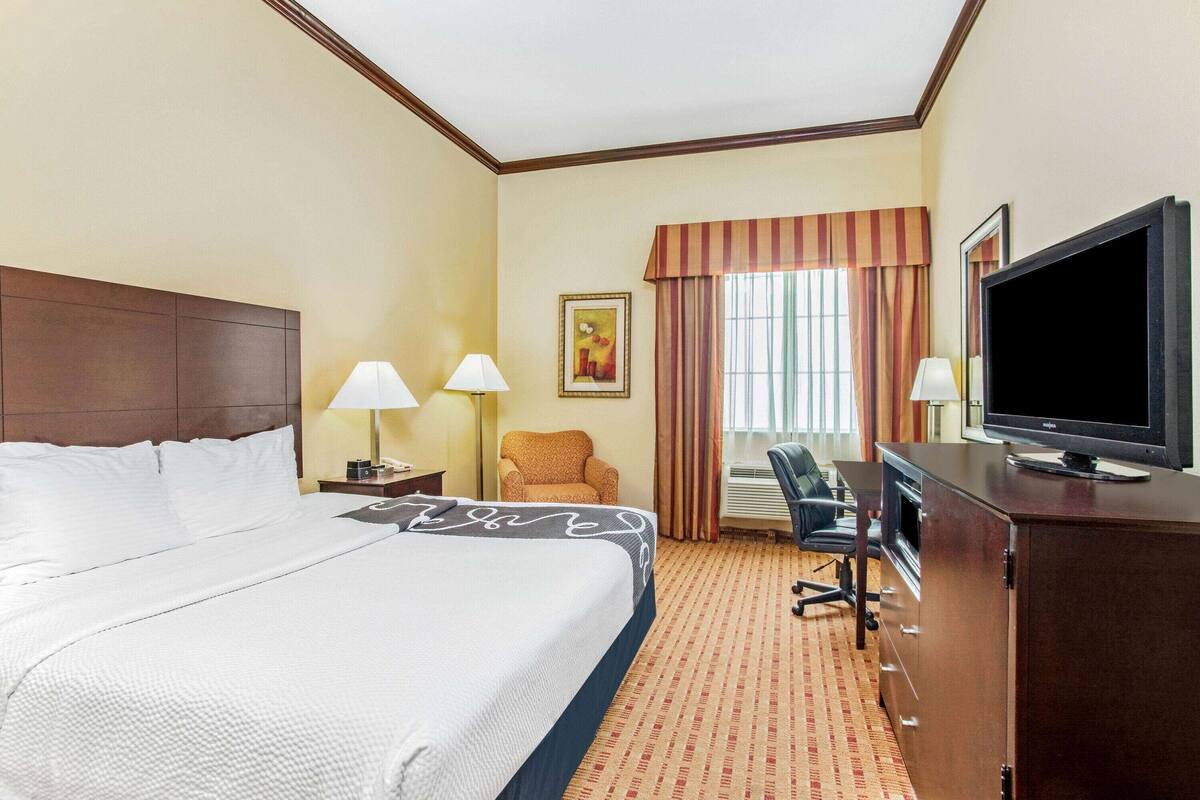 Ein Hotelzimmer mit einem großen Bett, einem Schreibtisch mit Computer, einem Fernseher und zwei Lampen.