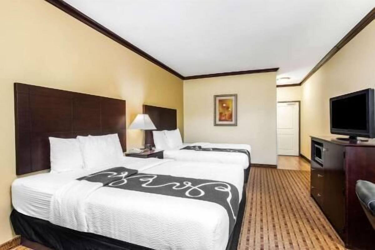 Ein Hotelzimmer mit zwei Betten, einem Fernseher, einem Schreibtisch und einem Bild an der Wand.