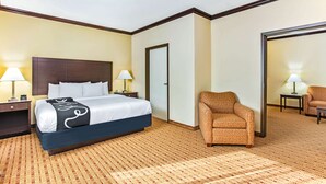 Une chambre d’hôtel avec un grand lit, deux tables de chevet avec des lampes, une moquette à motifs et un coin salon comprenant une chaise et un canapé.