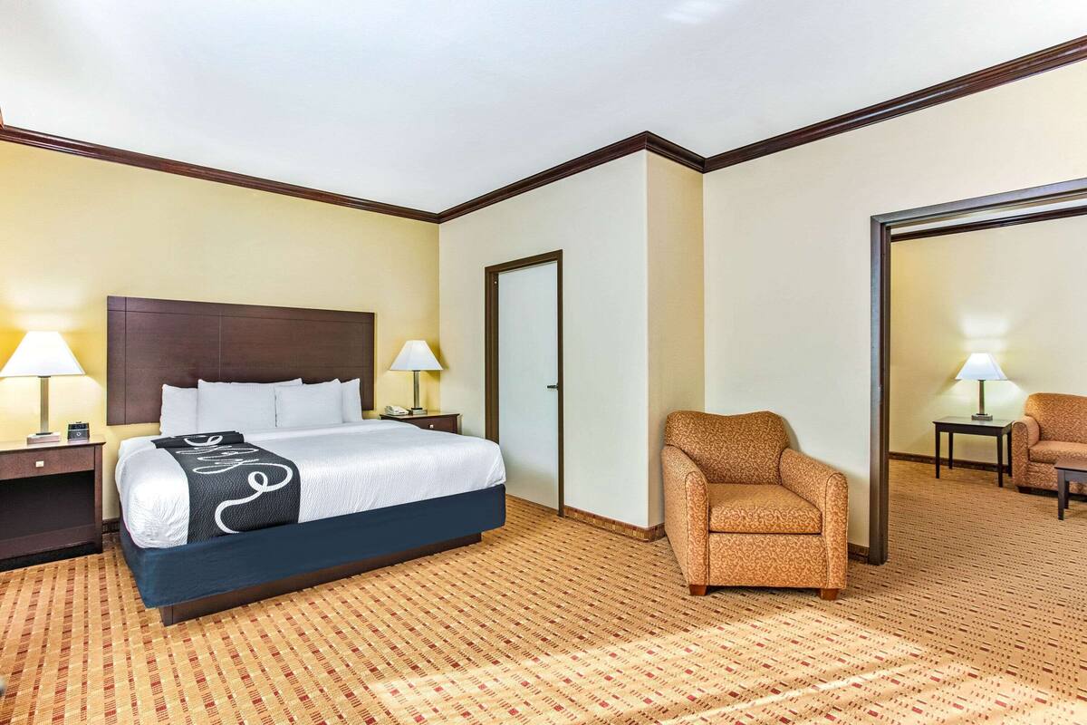Ein Hotelzimmer mit einem großen Bett, zwei Nachttischen mit Lampen, einem gemusterten Teppich und einer Sitzecke mit Sessel und Sofa.