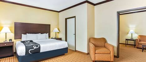 A hotel room with a large bed, two bedside tables with lamps, a patterned carpet, and a seating area with a chair and a sofa.
