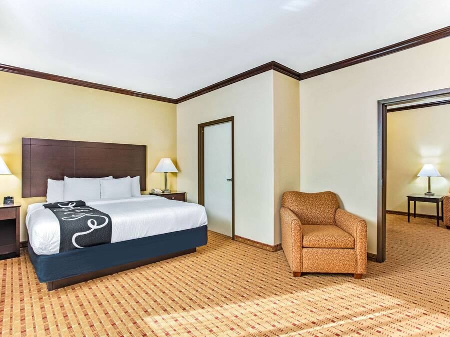 A hotel room with a large bed, two bedside tables with lamps, a patterned carpet, and a seating area with a chair and a sofa.