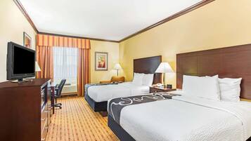 A hotel room with two beds, a desk with a television, a lamp, and a window with curtains.