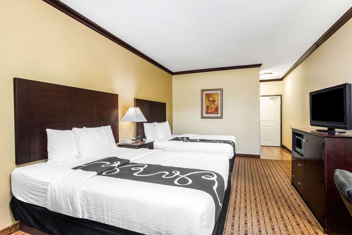 Ein Hotelzimmer mit zwei Betten, einem Fernseher, einem Schreibtisch und einem Bild an der Wand.