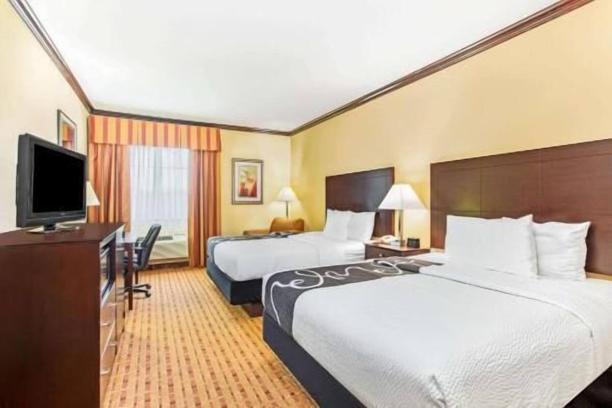 A hotel room with two beds, a desk with a TV, and a chair.