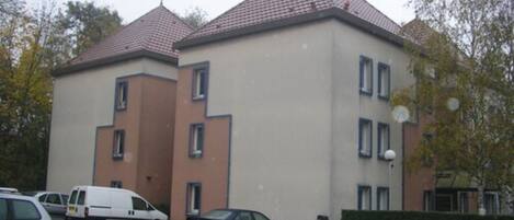 A multi-story building with a tiled roof, several windows, and a parking lot with cars.