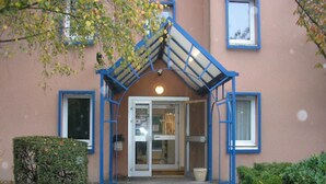 A building entrance with a blue metal archway, a glass door, and a small window. - Mister Bed Lomme (Lille)