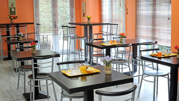 A dining area with multiple tables and chairs, some with breakfast items like toast and orange juice. - Mister Bed Lomme (Lille)