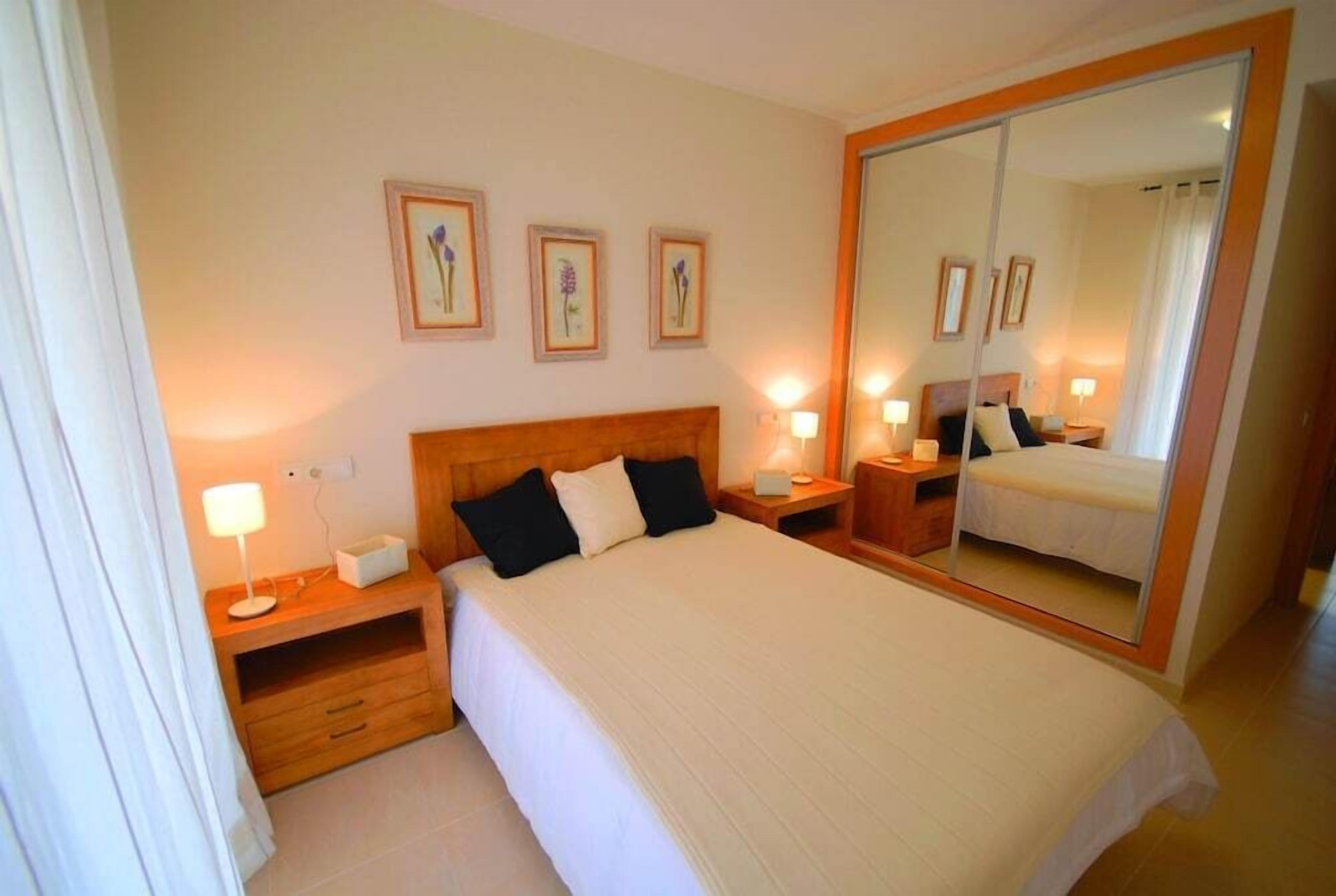 A hotel room with a large bed, bedside tables with lamps, a mirror, and framed floral artwork on the wall.