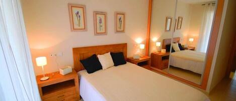 A hotel room with a large bed, bedside tables with lamps, a mirror, and framed floral artwork on the wall.