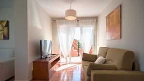 A living room with a sofa, TV, and a view of a building outside. - Apartamentos Paraiso Playa (Vera)
