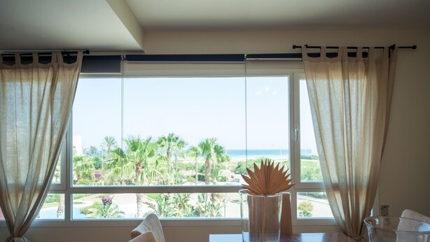 A room with a large window overlooking a beach, a vase with a decorative plant, and a table with a candle and a glass container. - Apartamentos Paraiso Playa (Vera)