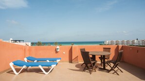 A terrace with a table and chairs, a pair of blue lounge chairs, and a view of the ocean. - Apartamentos Paraiso Playa (Vera)