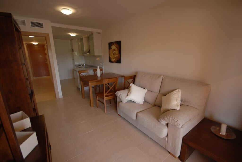 Una sala de estar con un sofá color beige, una mesa de comedor de madera y una cocina al fondo.