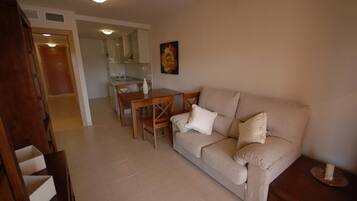 Una sala de estar con un sofá color beige, una mesa de comedor de madera y una cocina al fondo.