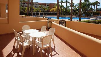 A terrace with a pool view, white furniture, and palm trees.