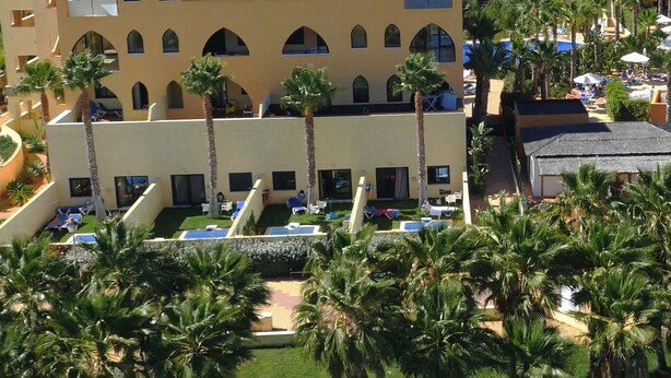 A hotel with multiple floors, outdoor swimming pools, and palm trees. - Apartamentos Playamarina (Ayamonte)