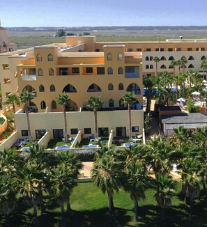 Un hotel con varios pisos, piscinas exteriores y palmeras.