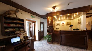 A reception area with a wooden desk, a computer, a potted plant, and a mounted fox. - Hotel Santa San (Ayas)