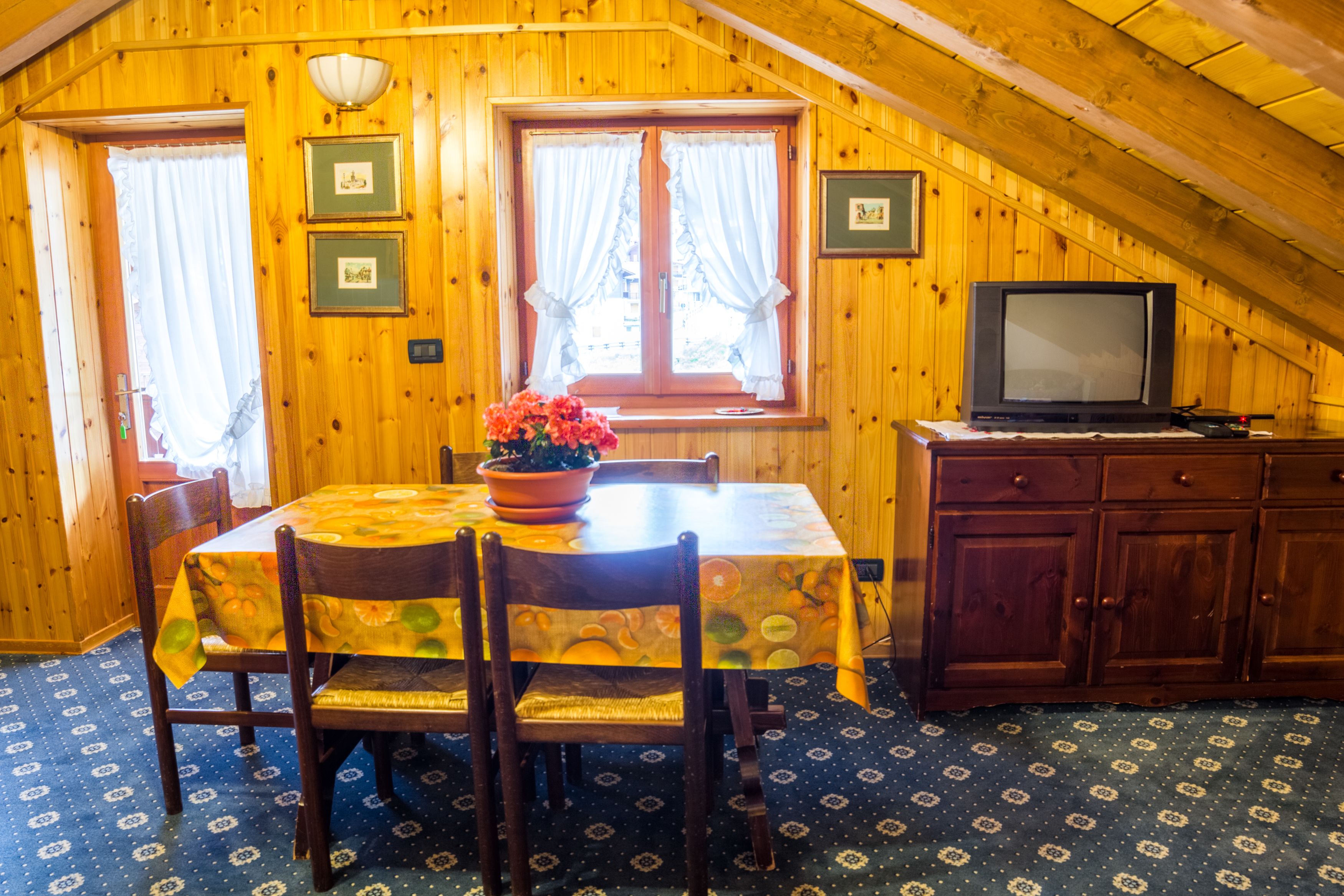 Un comedor con una mesa dispuesta para dos, un televisor y un aparador.