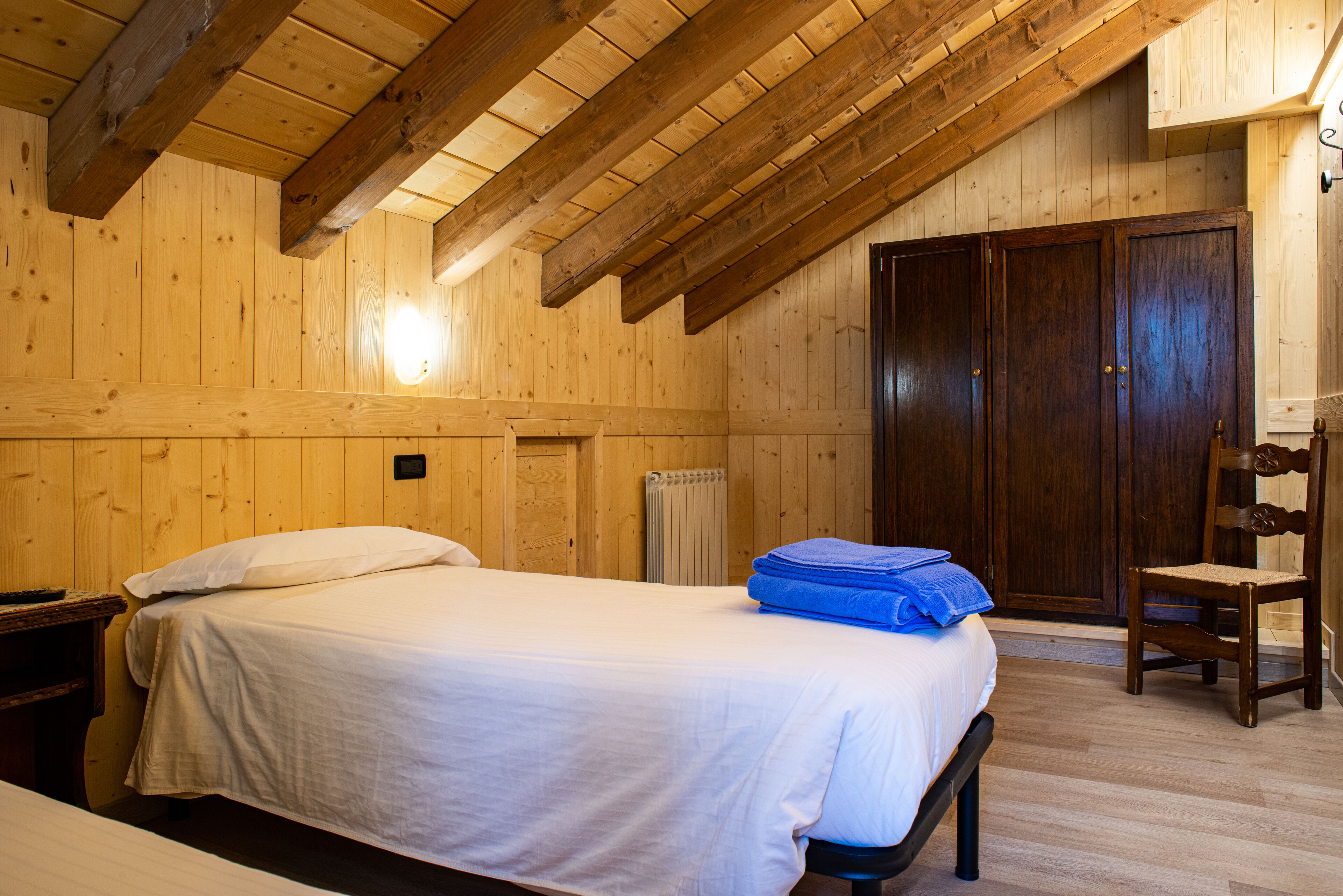 A wooden room with a bed, a chair, and a wardrobe.