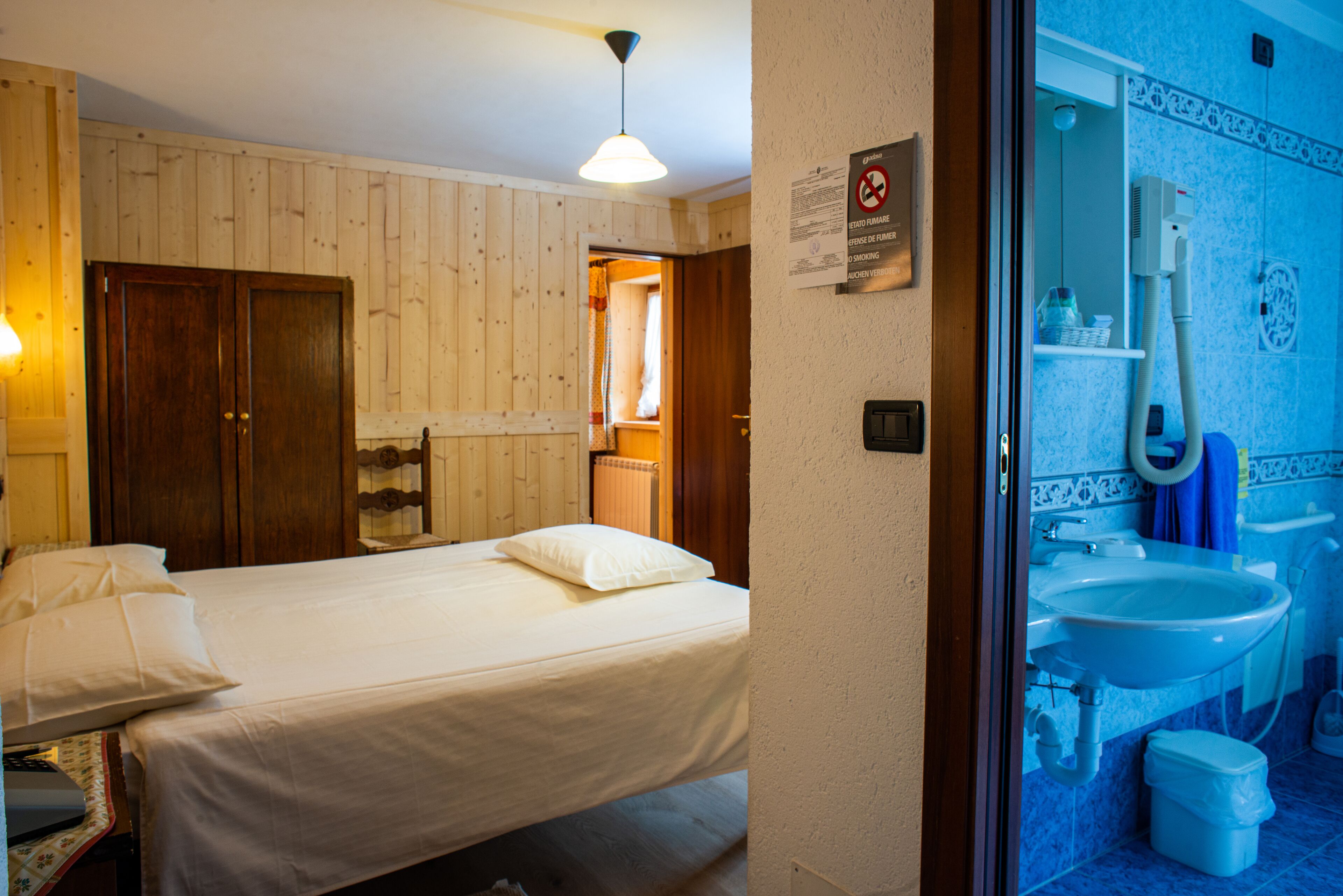 A bedroom with a bed, wooden wardrobe, and a bathroom with a sink and toilet.