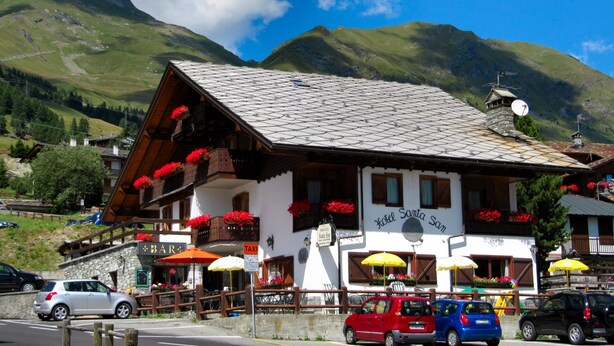 A mountain-view hotel with outdoor seating and a sign reading "Hotel Santa Sam". - Hotel Santa San (Ayas)