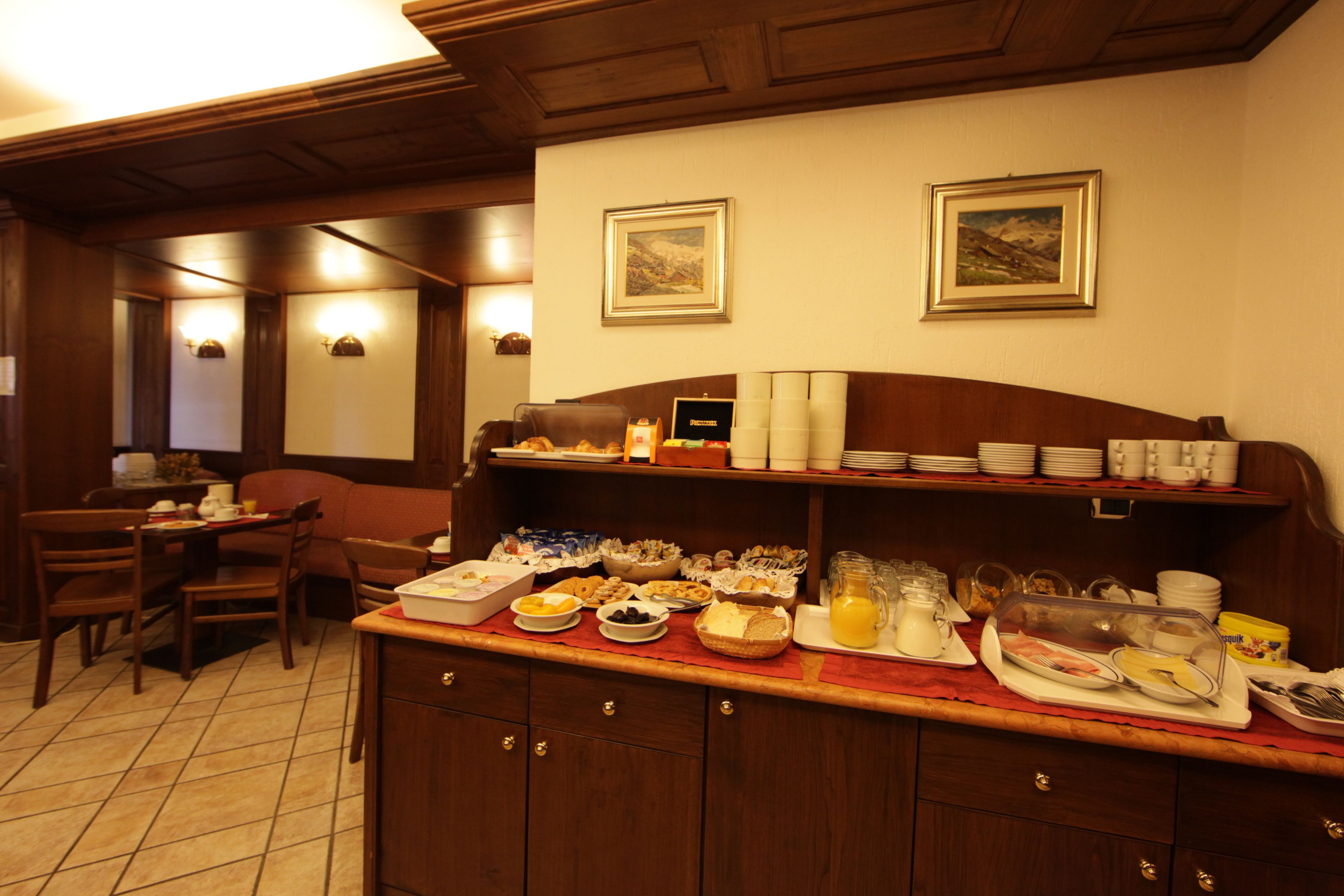 A breakfast buffet with various food items and beverages, wooden furniture, and framed pictures on the wall.
