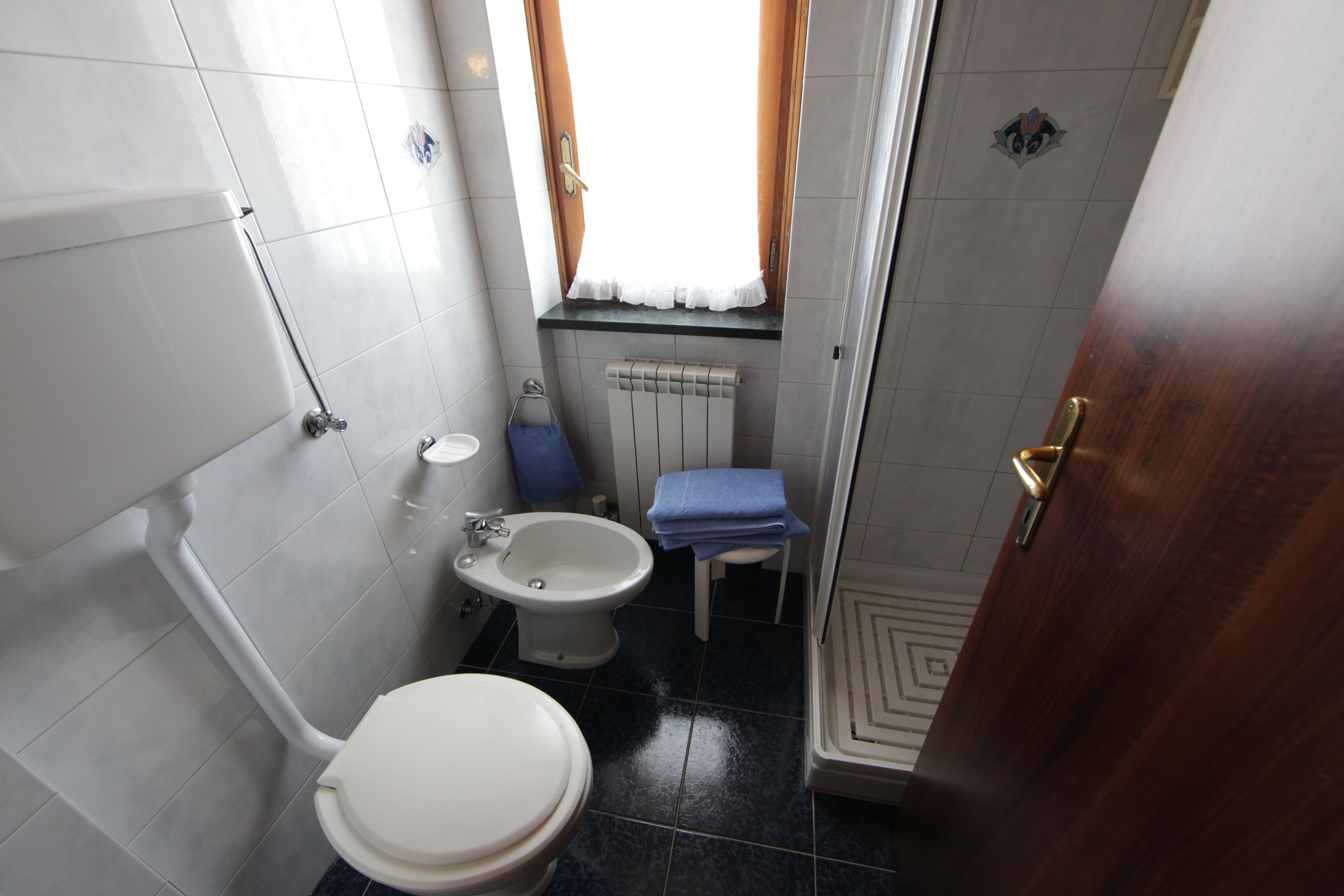 Une petite salle de bain comprenant des toilettes, un bidet, un lavabo et une petite fenêtre avec des rideaux.