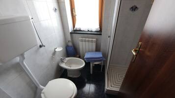 A compact bathroom with a toilet, bidet, sink, and a small window with curtains.