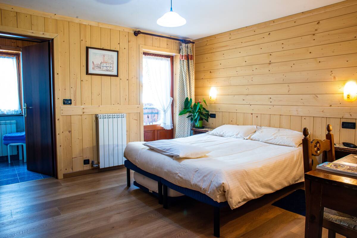 A wooden-paneled room with a bed, a table with a book, and a plant.