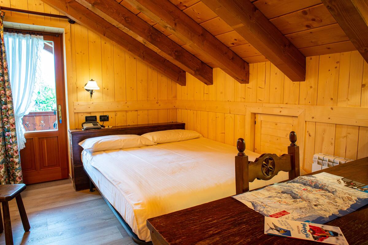A wooden cabin room with a bed, a nightstand, a lamp, and a table with a map.