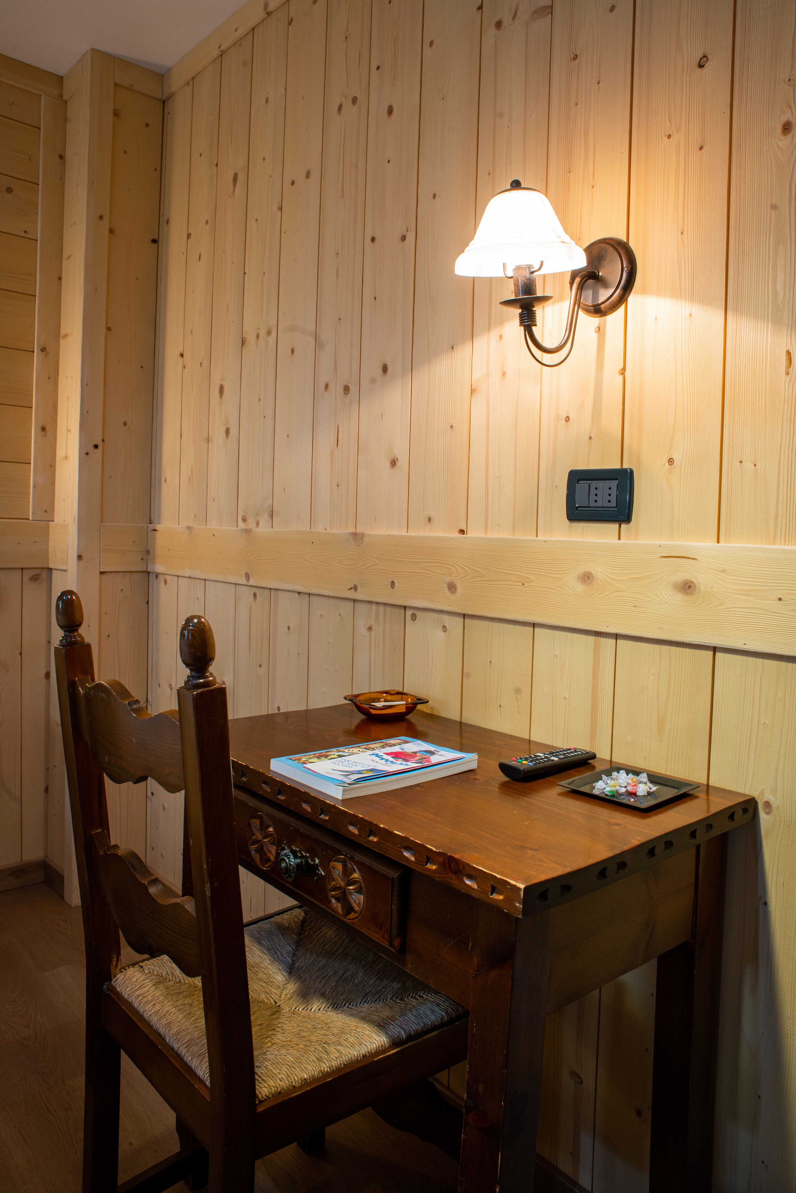 A wooden dining table with a lamp, a remote control, and a bowl.