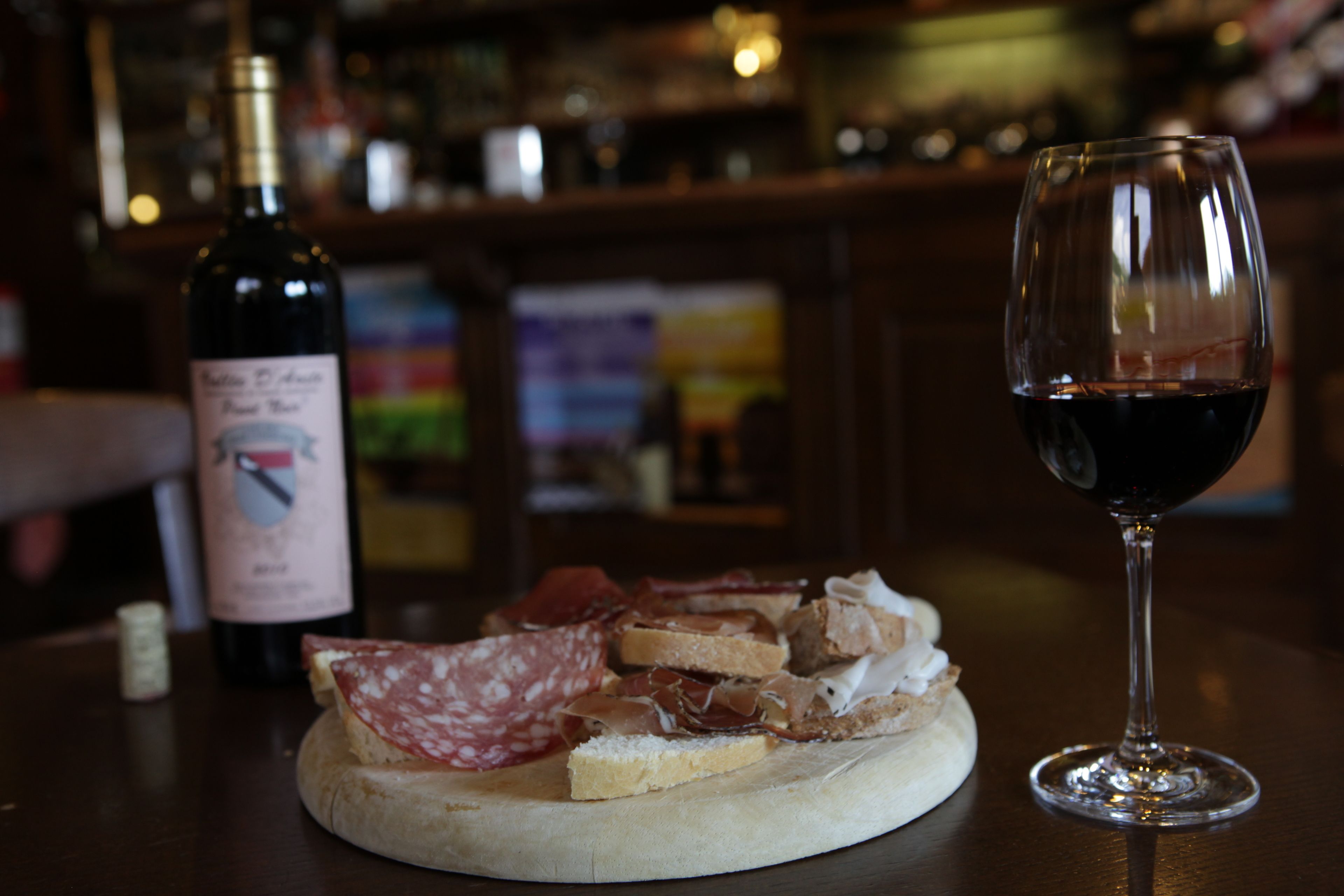 Uma mesa redonda de madeira com um copo de vinho tinto e uma garrafa de vinho.