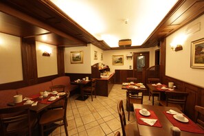 A dining area with wooden furniture, a central island with a sink, and a staircase leading to an upper level. - Hotel Santa San (Ayas)
