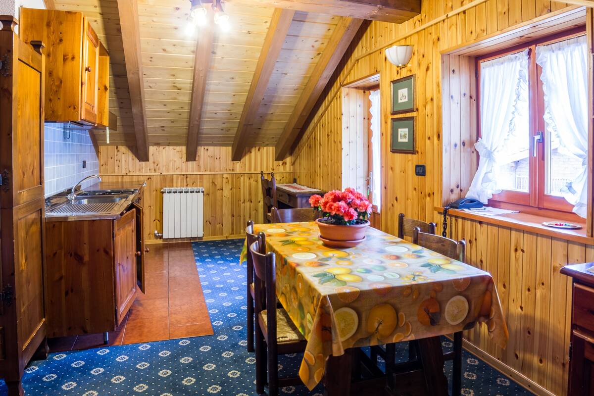 A wooden cabin with a kitchen, dining area, and a window with curtains.