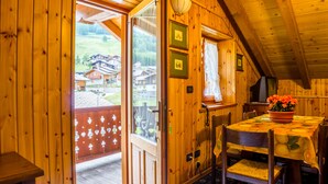A wooden cabin with a dining area featuring a table with a floral tablecloth and chairs. - Hotel Santa San (Ayas)