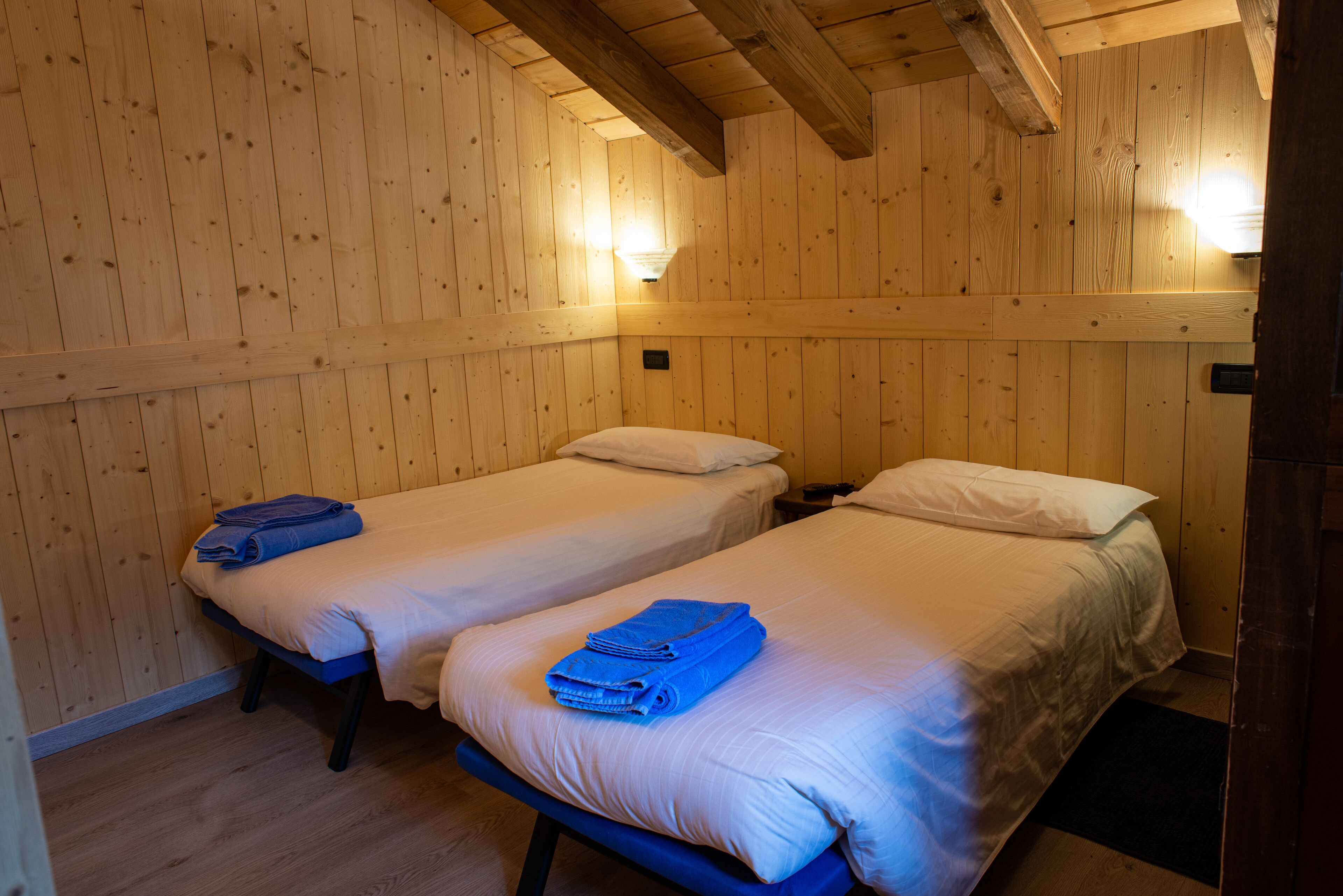 A room with two single beds, wooden walls, and a sloped ceiling.
