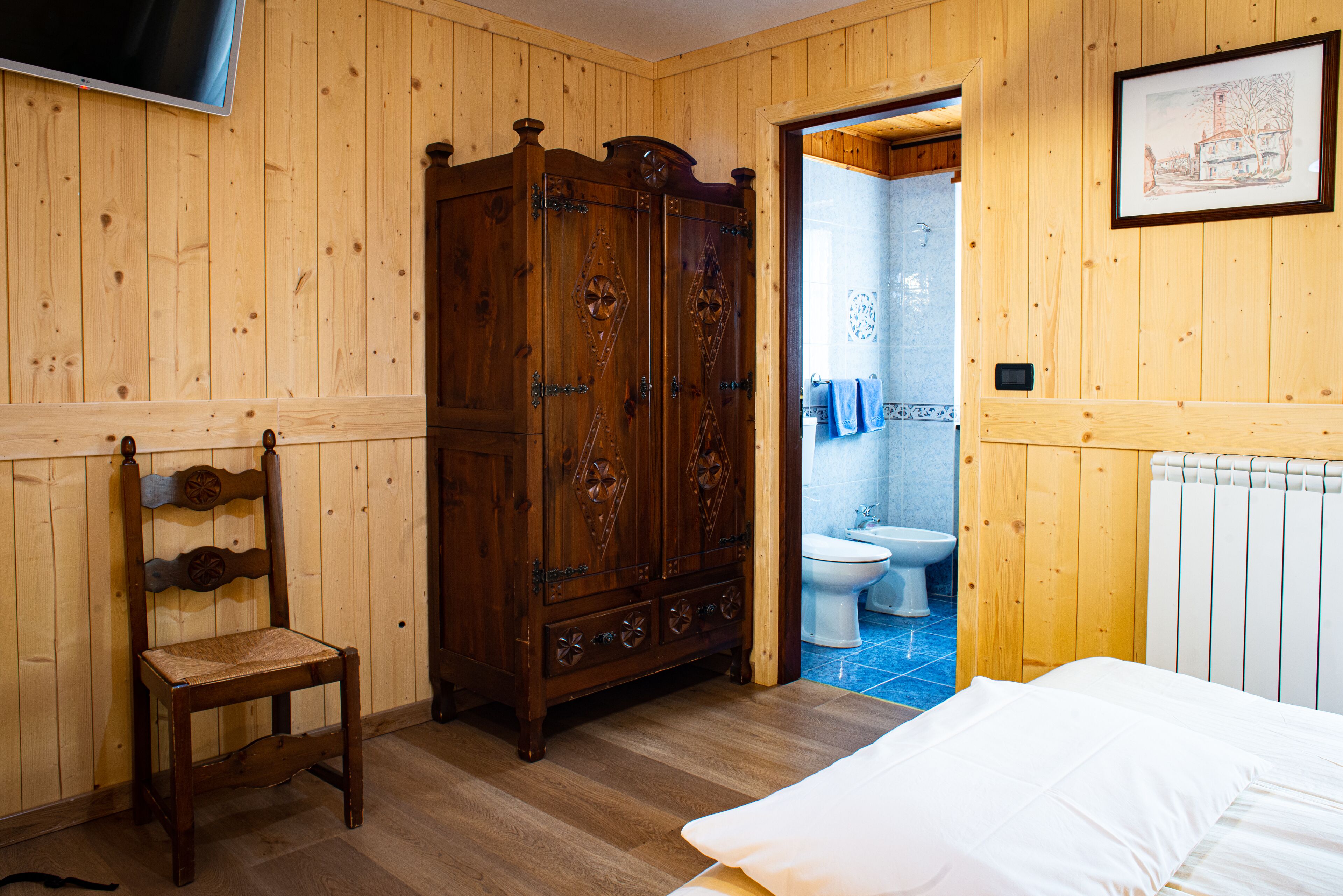 A wooden-paneled room with a bed, a wooden wardrobe, and a chair.