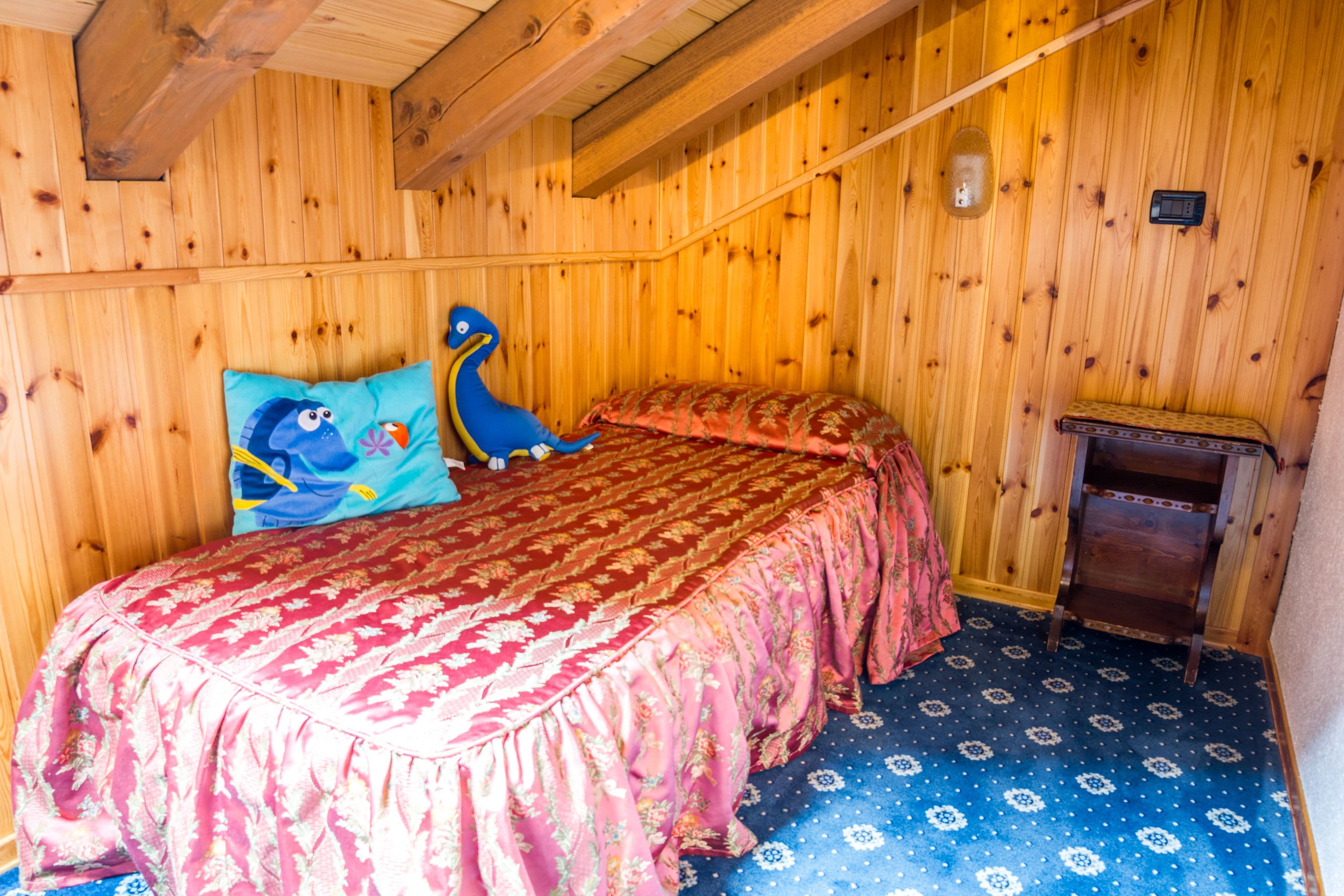 Una habitación con paneles de madera, una cama, una mesita de noche de madera y una alfombra azul estampada.