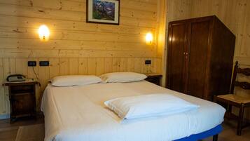 A wooden-paneled room with a bed, two bedside lamps, a wooden wardrobe, and a chair.