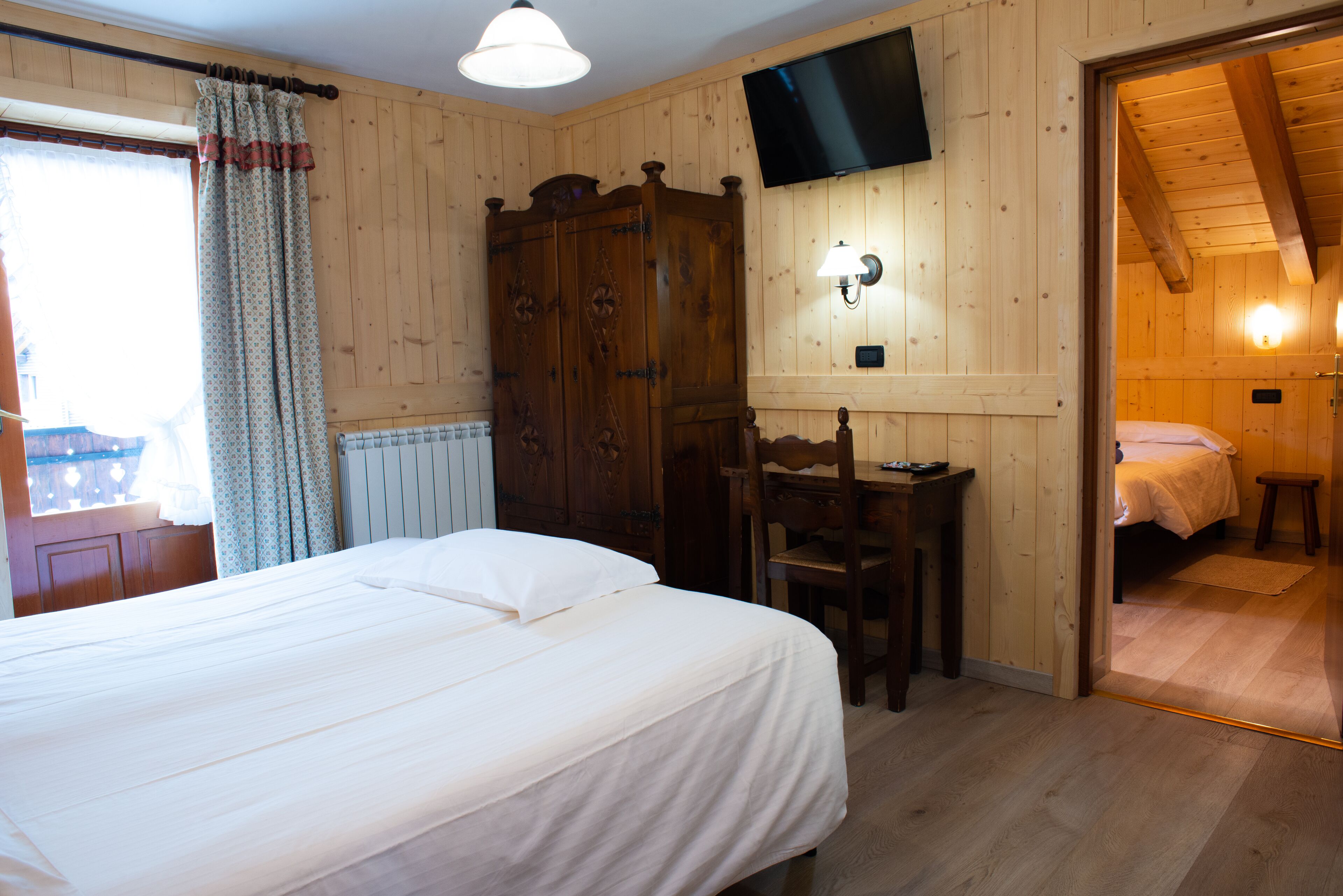 A wooden-paneled room with a bed, a desk, and a TV mounted on the wall.